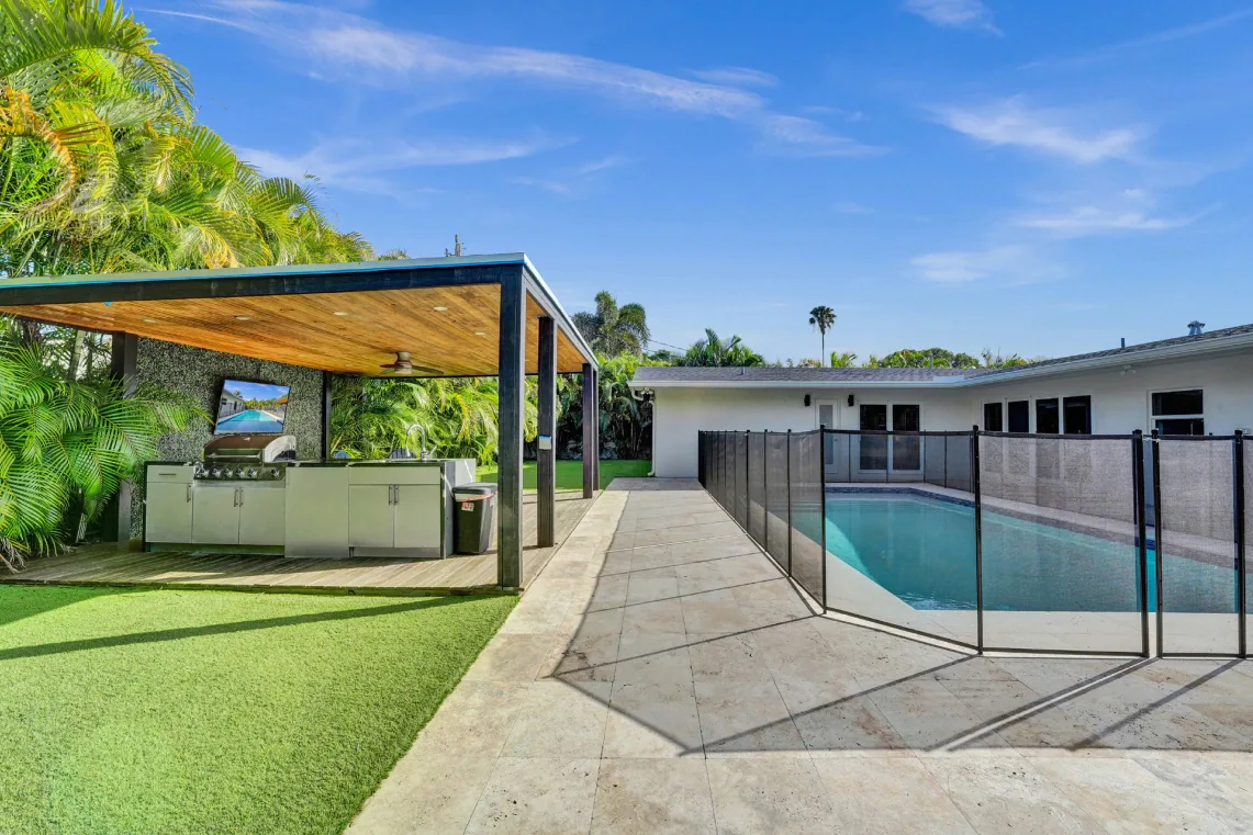 Backyard with covered outdoor kitchen, pergola, artificial turf, and fenced pool
