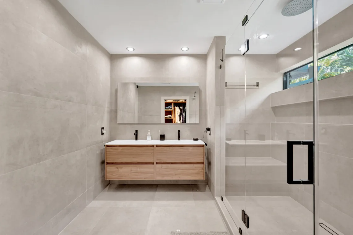 Modern bathroom with floating double wood vanity, large-format tile, and frameless glass shower
