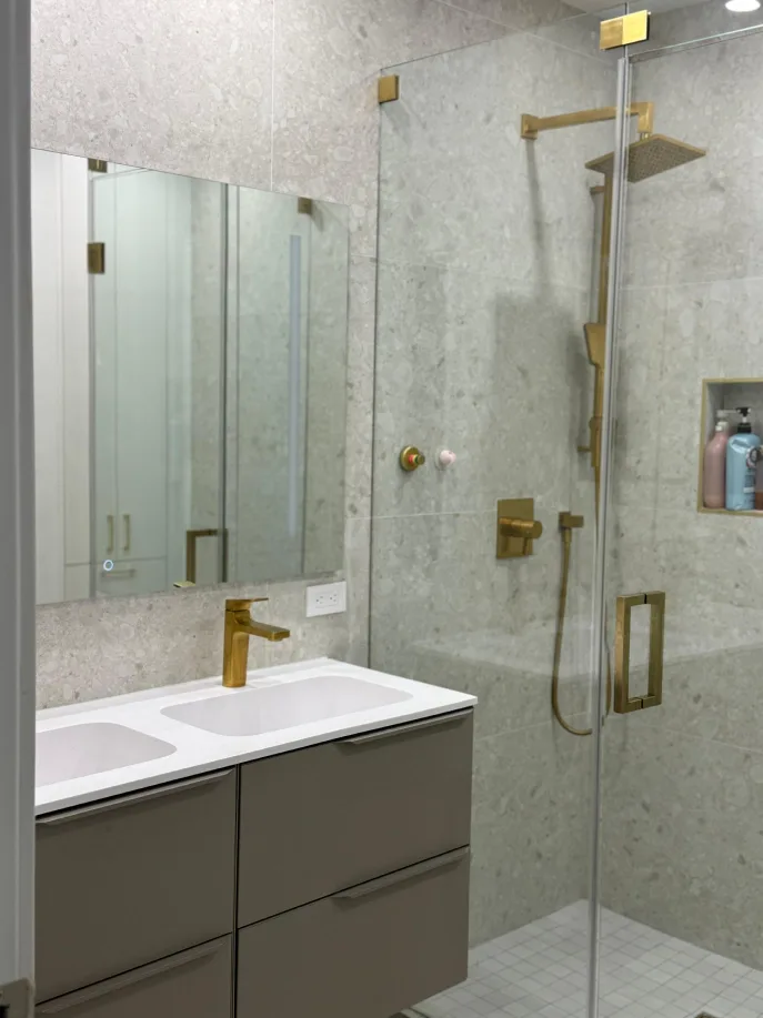 Stone-tiled bathroom with gold fixtures, glass shower, and floating double vanity