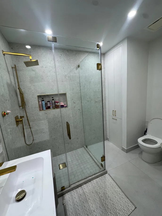 Marble bathroom with gold rainfall shower, glass enclosure, and wall-hung toilet