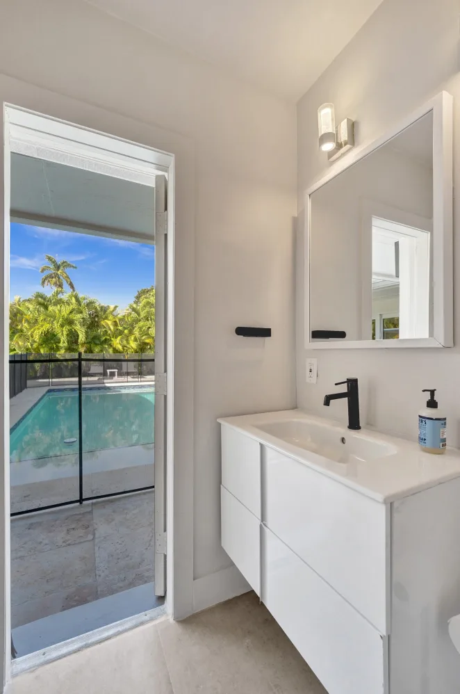 White floating vanity bathroom with framed mirror and door opening to pool