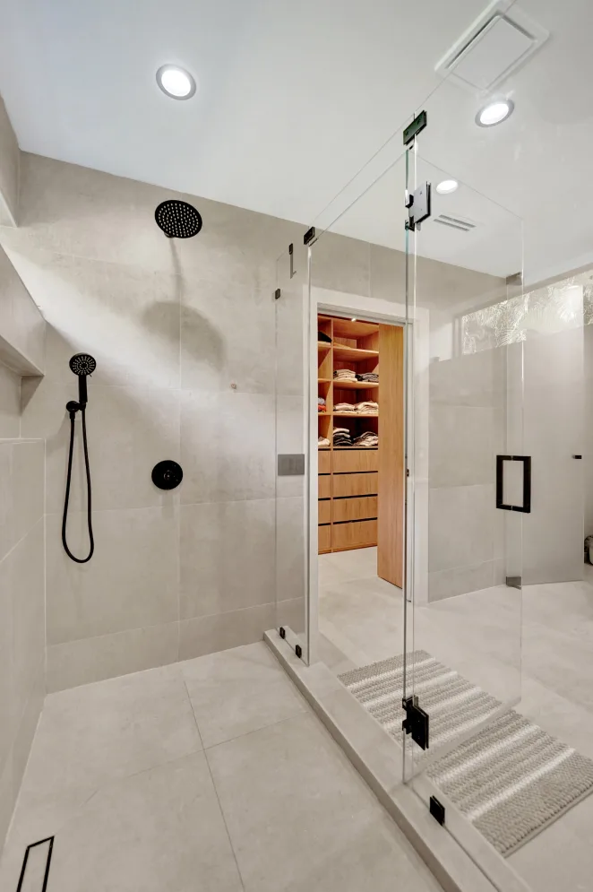 Walk-in glass shower with rainfall heads and view into wood walk-in closet