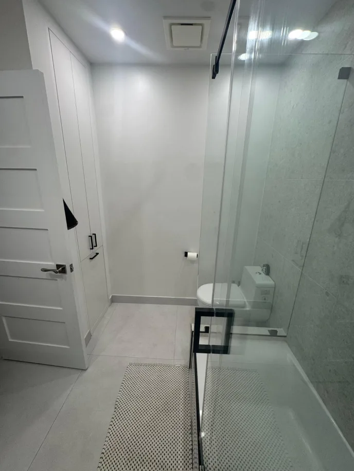 Clean white bathroom with marble glass shower, toilet, and linen closet