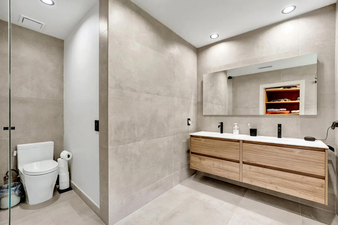 Spacious bathroom with floating wood vanity, large mirror, toilet, and glass shower
