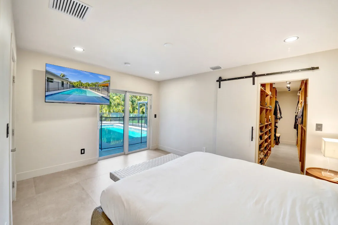 Bright bedroom with sliding-door pool view, wall-mounted TV, and barn-door walk-in closet