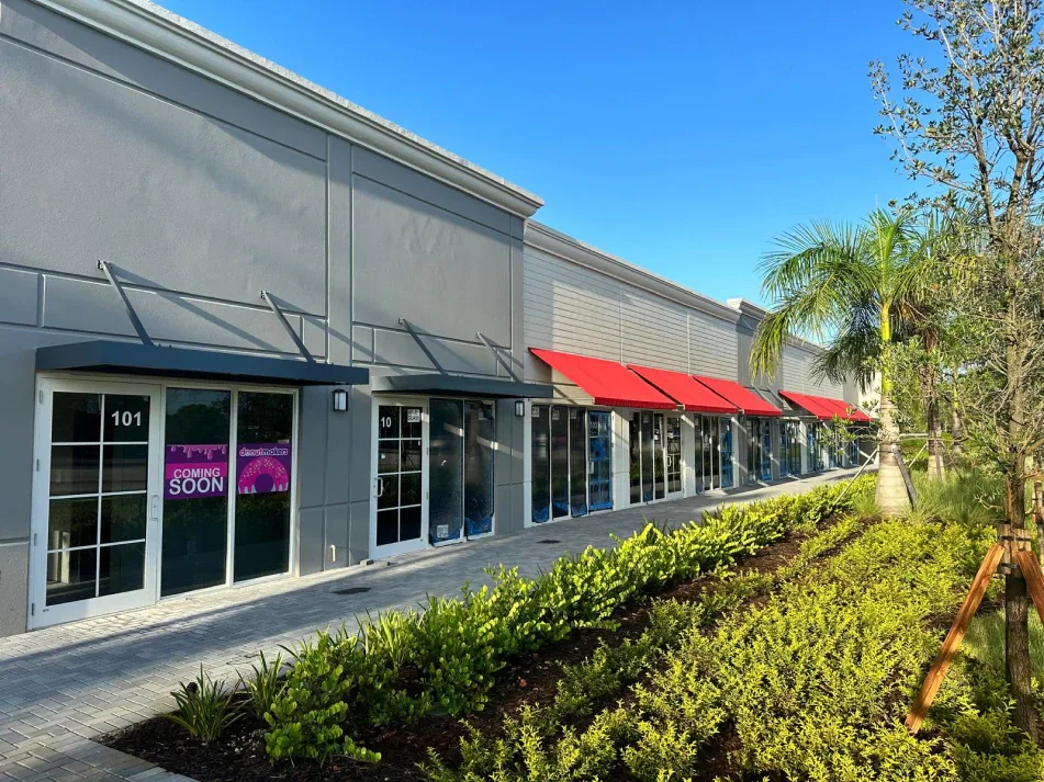 Gray retail building corner with red awnings and paver walkway under cloudy sky