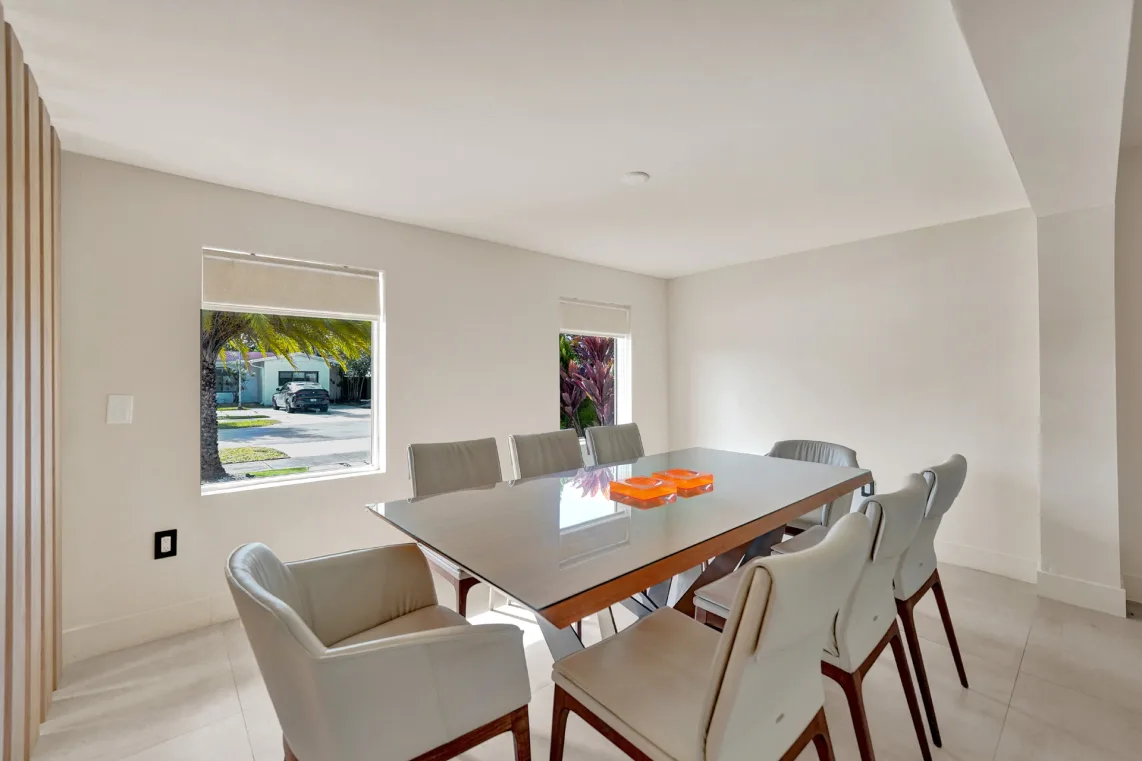 Bright dining room with glass-top wood table, cream chairs, and street-facing windows