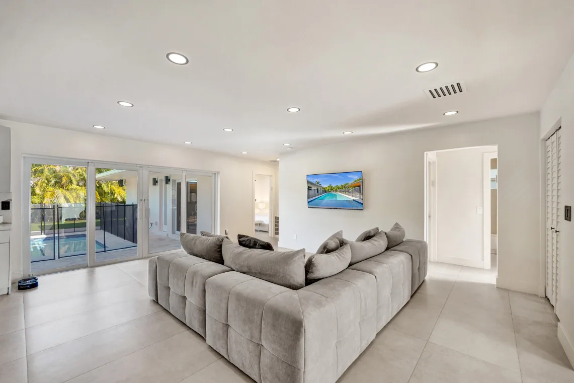 Spacious family room with gray sectional, wall-mounted TV, and pool-view sliding doors