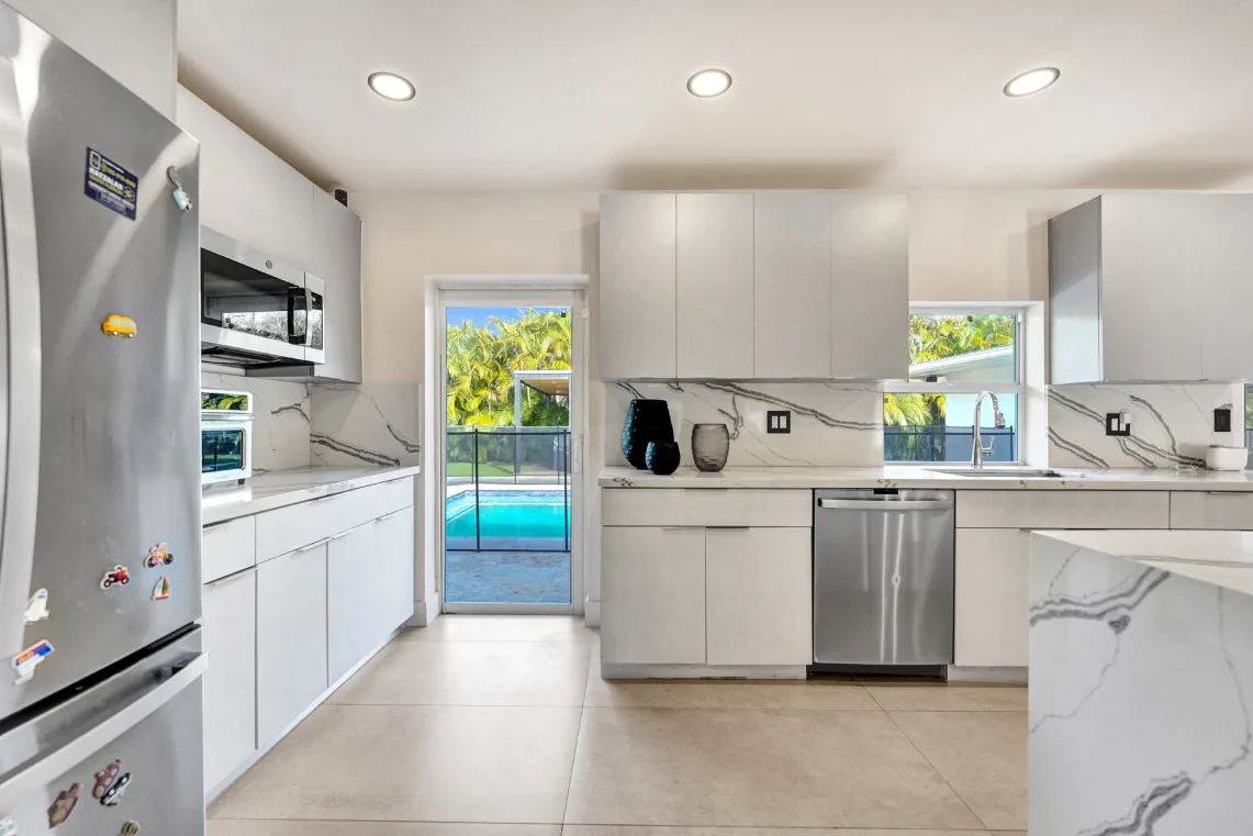 Bright white galley kitchen with marble counters and door opening to backyard pool
