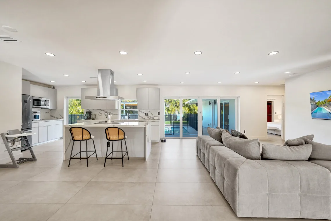 White kitchen island with cane bar stools open to a large living room