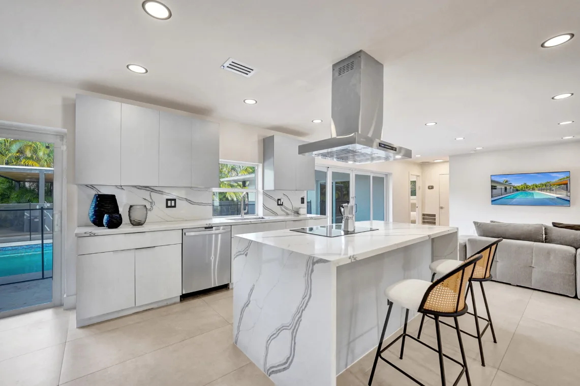 Modern kitchen with marble island, cane bar stools, and pool view beyond
