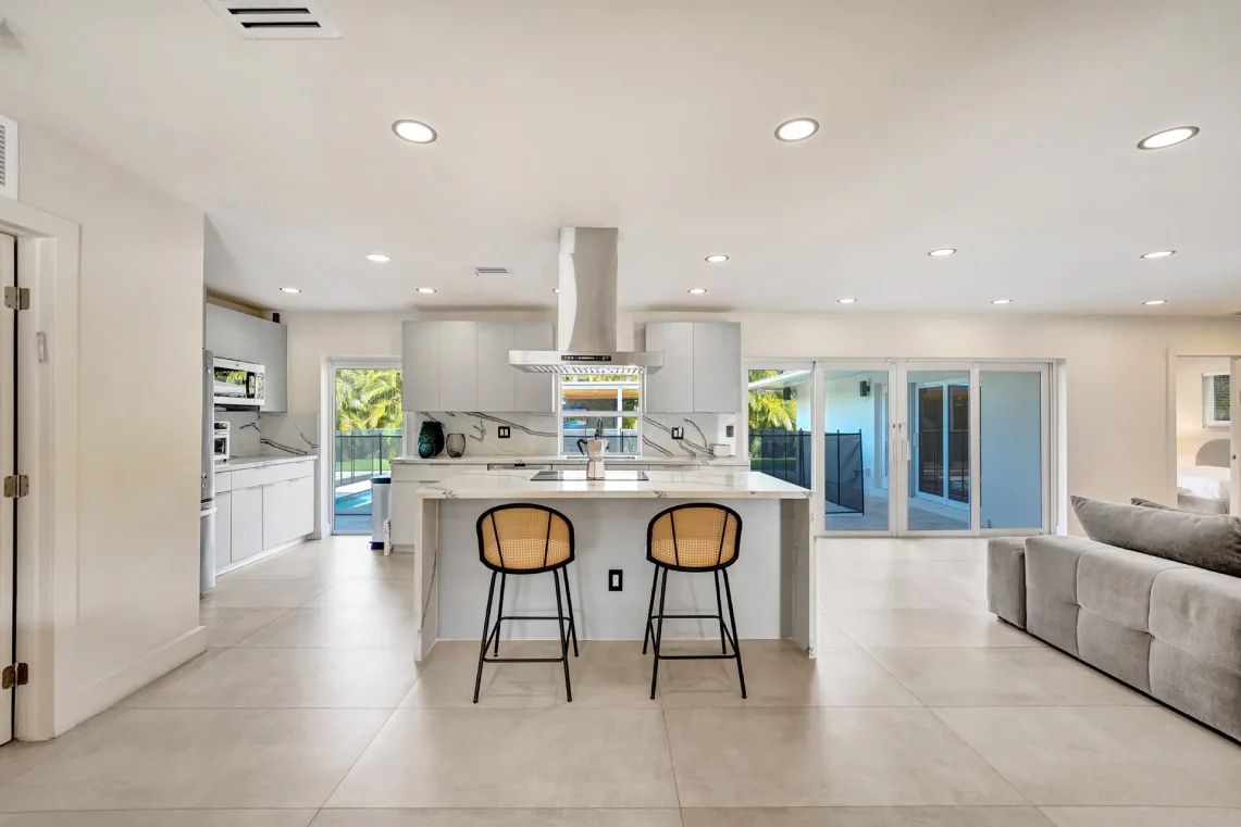 White kitchen with marble island, cane stools, stainless hood, and pool-view sliders