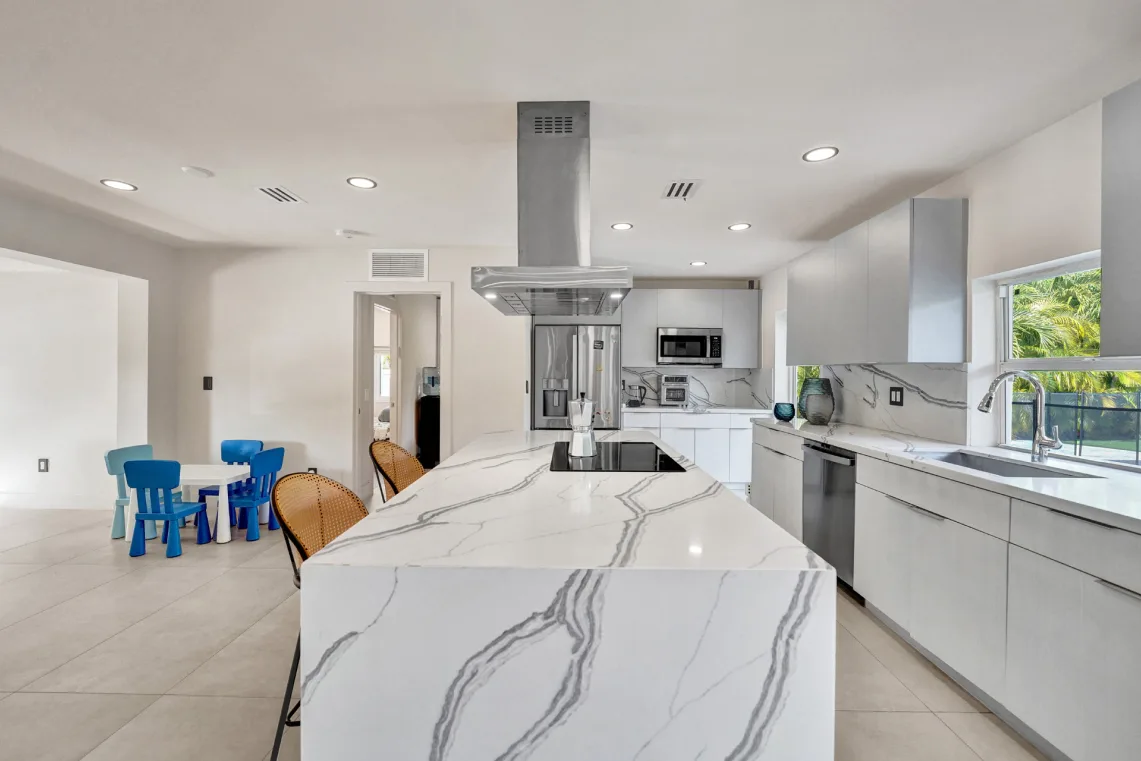 White kitchen with marble waterfall island, stainless hood, and children's play nook