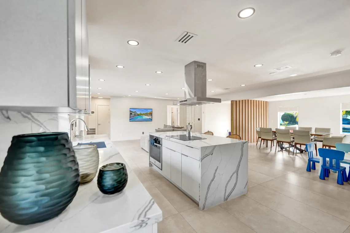 Open-concept kitchen with marble waterfall island and stainless island hood in Miami, FL