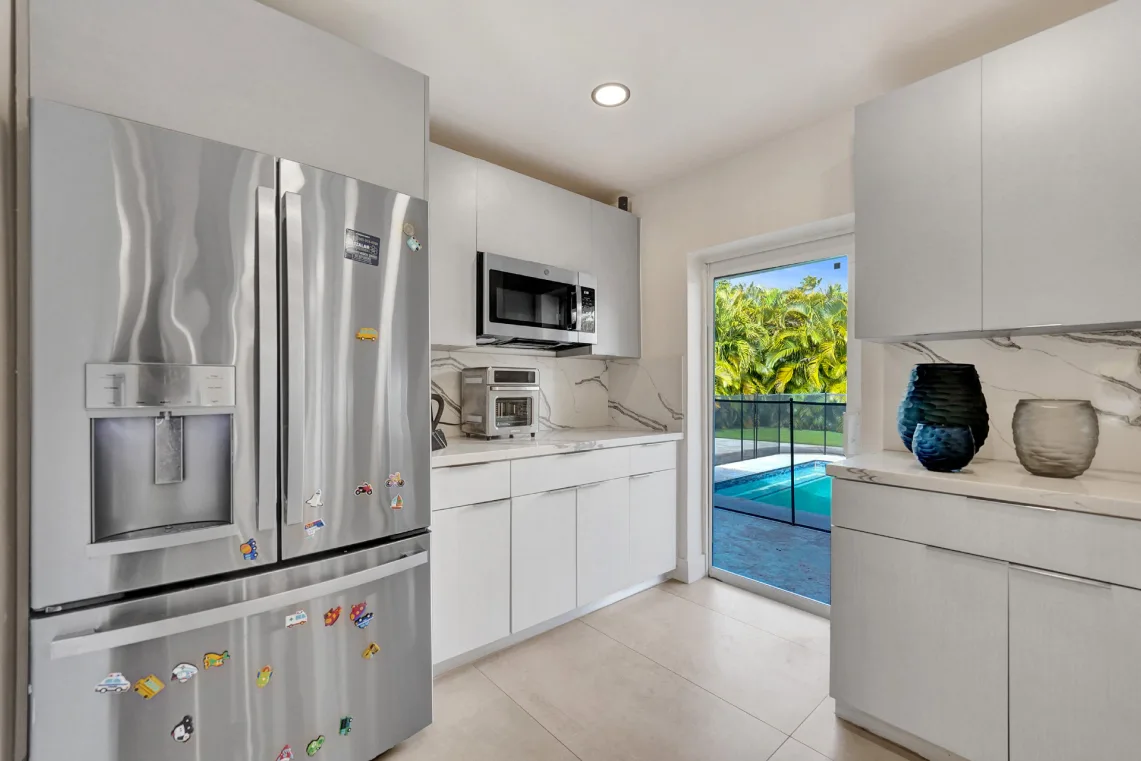 Kitchen pantry area with stainless refrigerator, marble backsplash, and door to pool