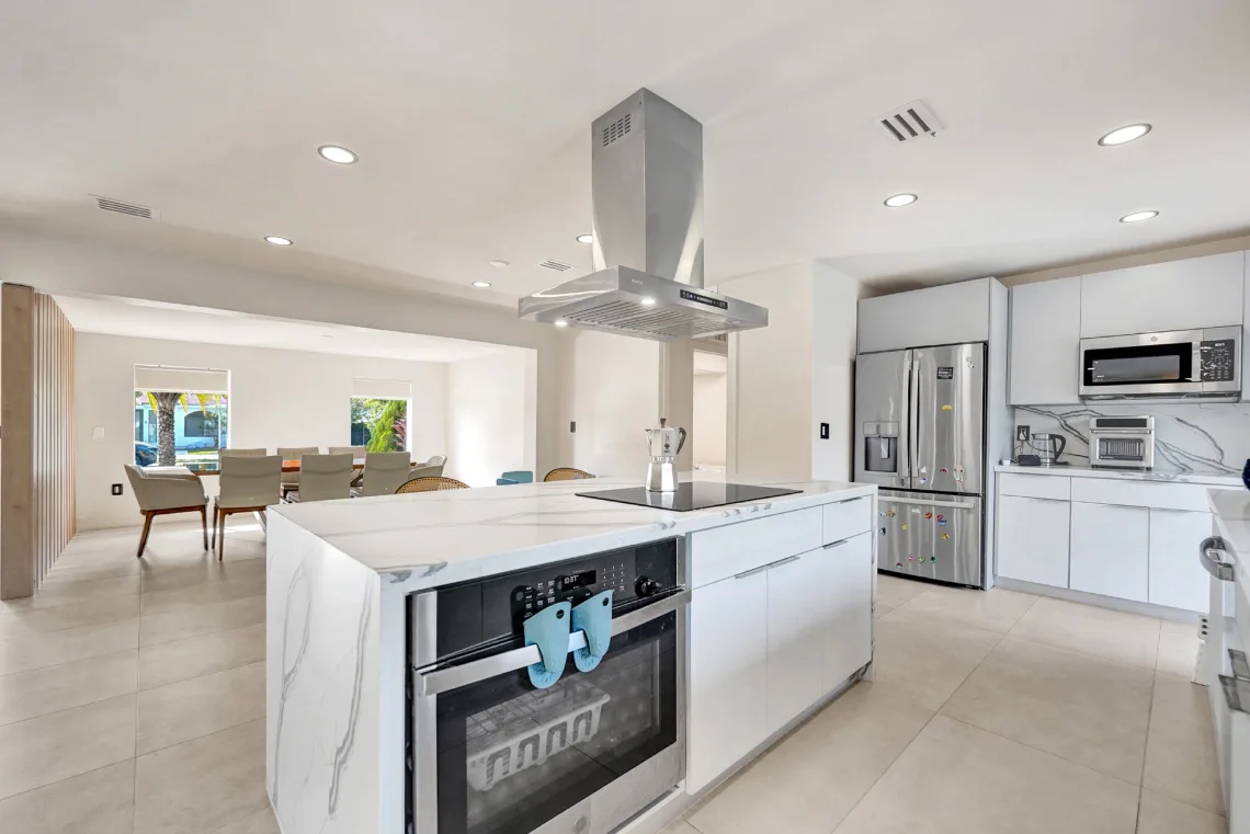 Modern white kitchen with waterfall marble island, stainless hood, and open dining area