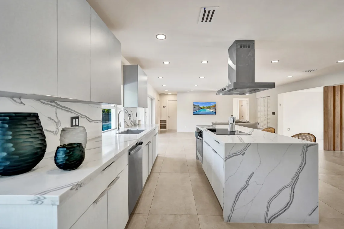 Sleek white kitchen with veined quartz island, stainless hood, and open floor plan