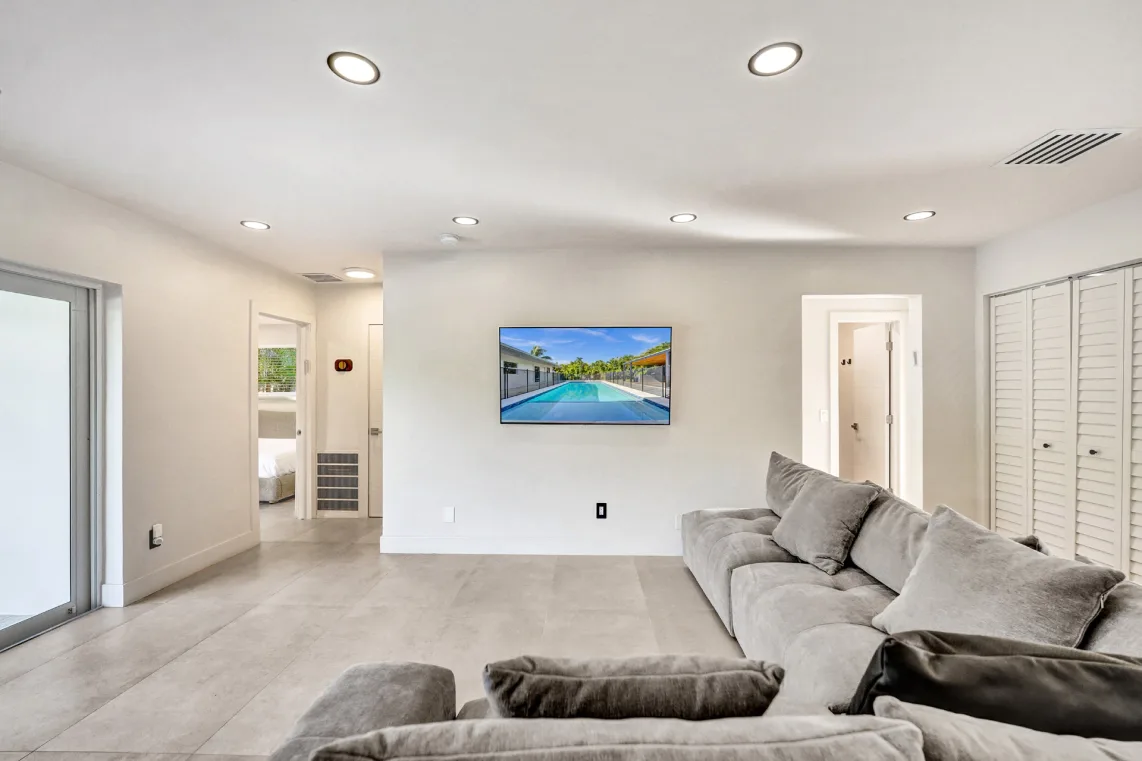Bright living room with plush gray sectional, wall TV, and hallway to bedrooms