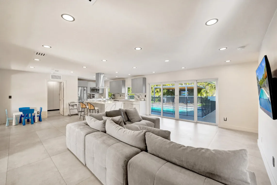 Open living room with large gray sectional, recessed lighting, and pool-view sliders