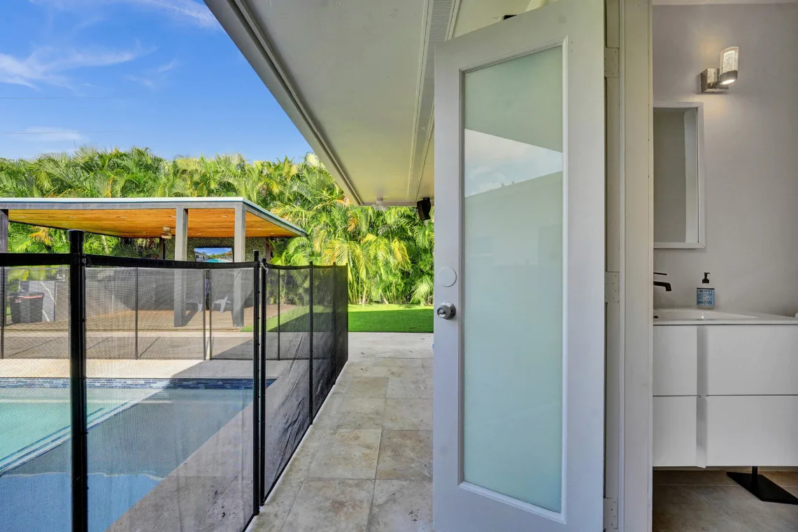 Poolside stone patio with wood cabana, safety fence, and adjacent outdoor half bath