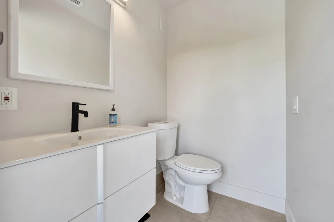 Compact powder room with white floating vanity, black faucet, mirror, and toilet