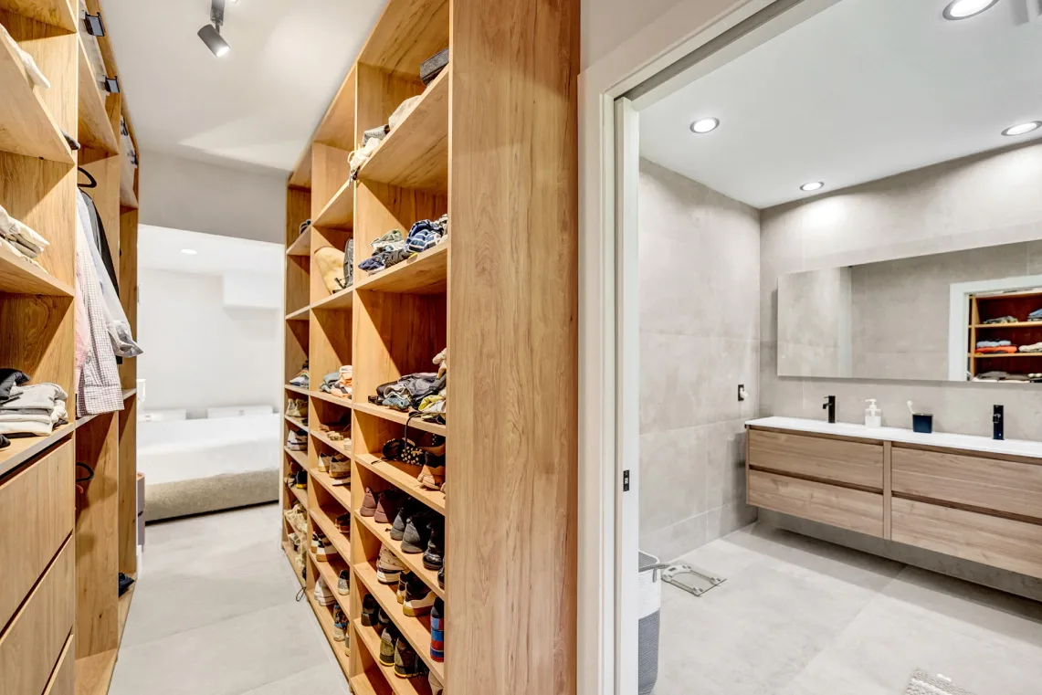 Wood walk-in closet with built-in shelving opening to an adjoining tiled bathroom